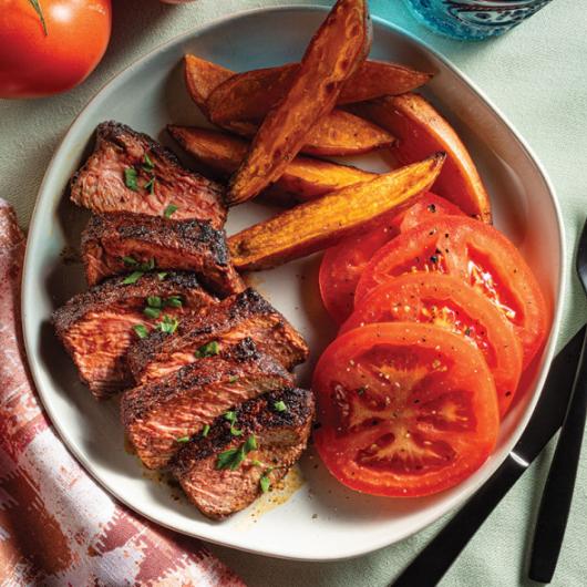 6 slices of coffee rubbed steak, sweet potato wedges, and sliced tomatoes on a plate