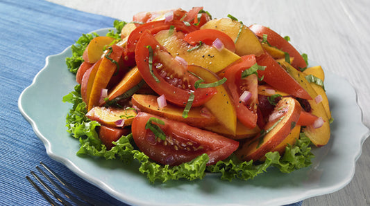 Sliced tomatoes and peaches on top of lettuce greens