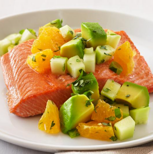 Salmon filet on a plate topped with diced avocado and oranges