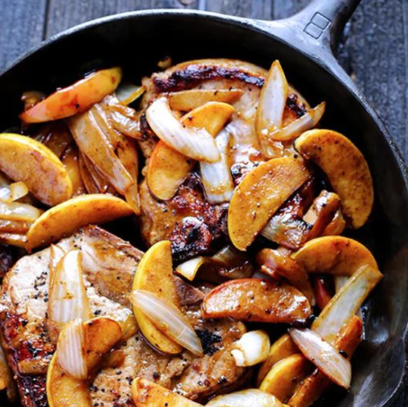 Skillet filled with pork chops, onions, and sliced peaches