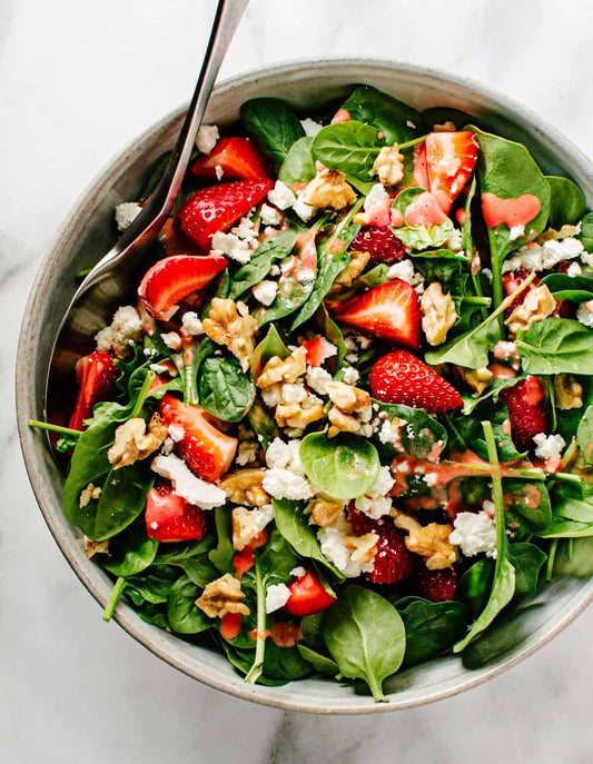 Bowl filled with salad of spinach, cheese, strawberries and nuts