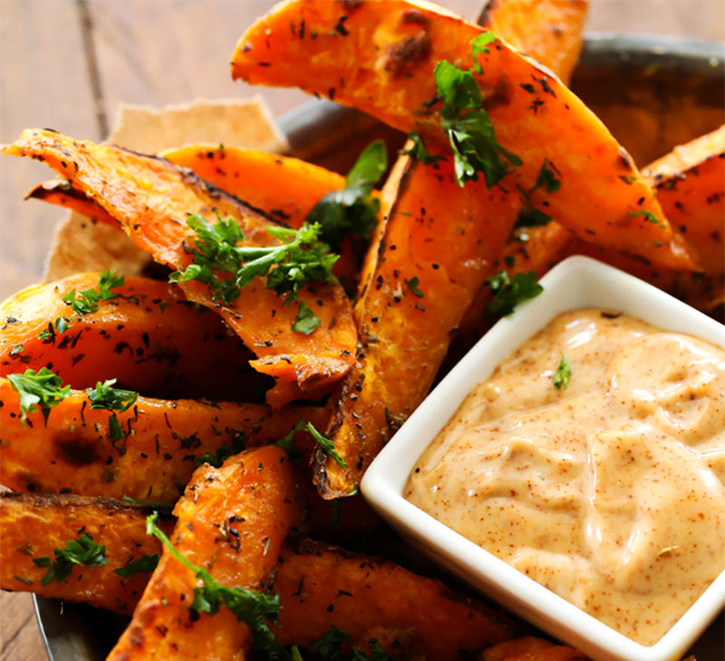 Roasted sweet potato wedges toped with seasonings and fresh cilantro with a cup of sauce on the side